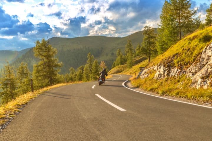 A Man Rides Along The Highway Among The Mountains